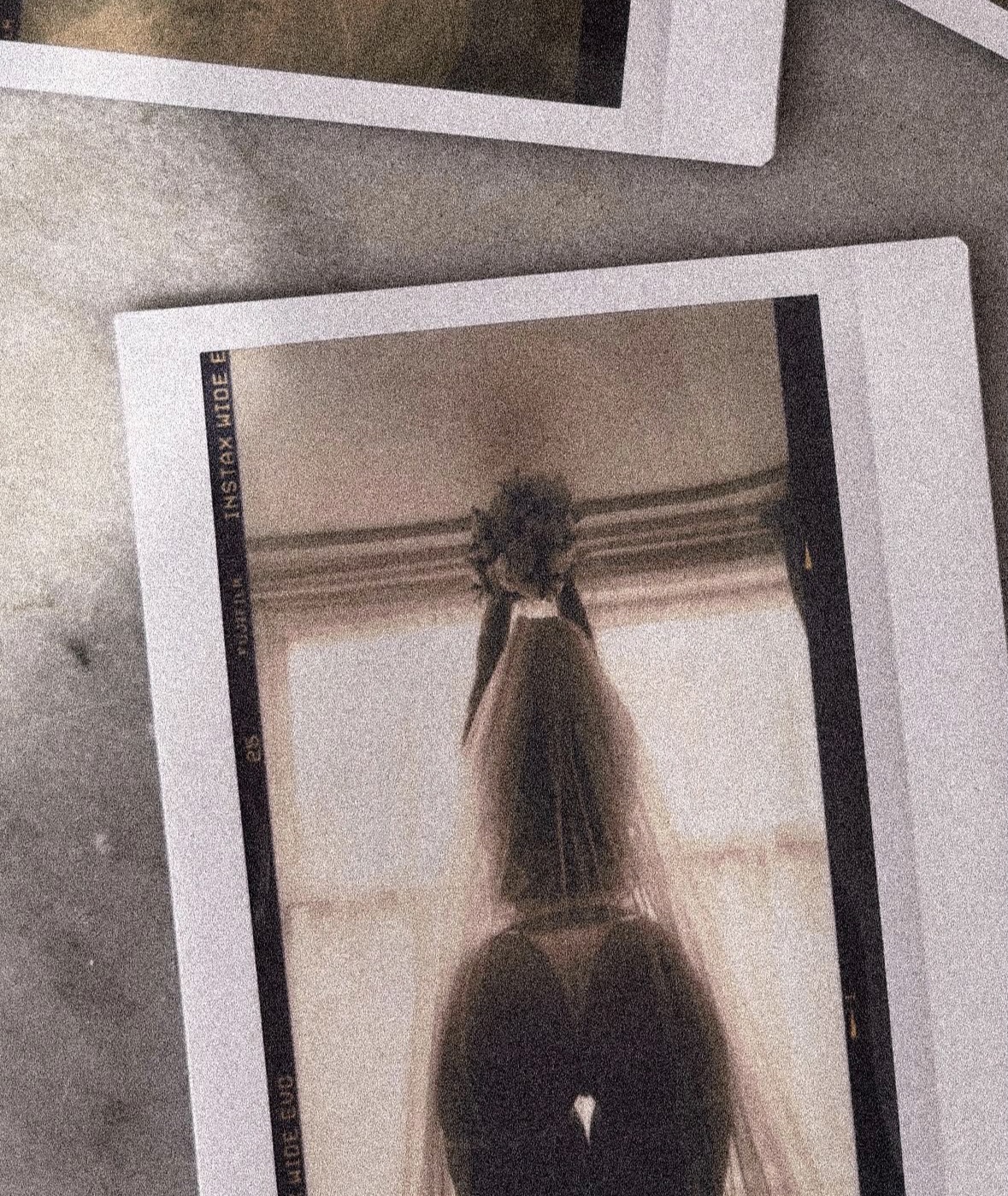 A veiled figure holding a bouquet of dark flowers against a bright window, Instax film print